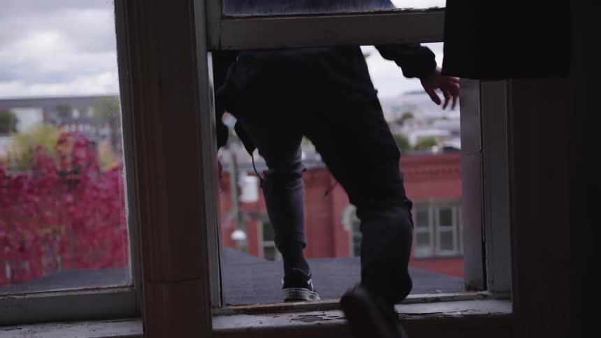 Man sitting on a windowsill looking out at city rooftops