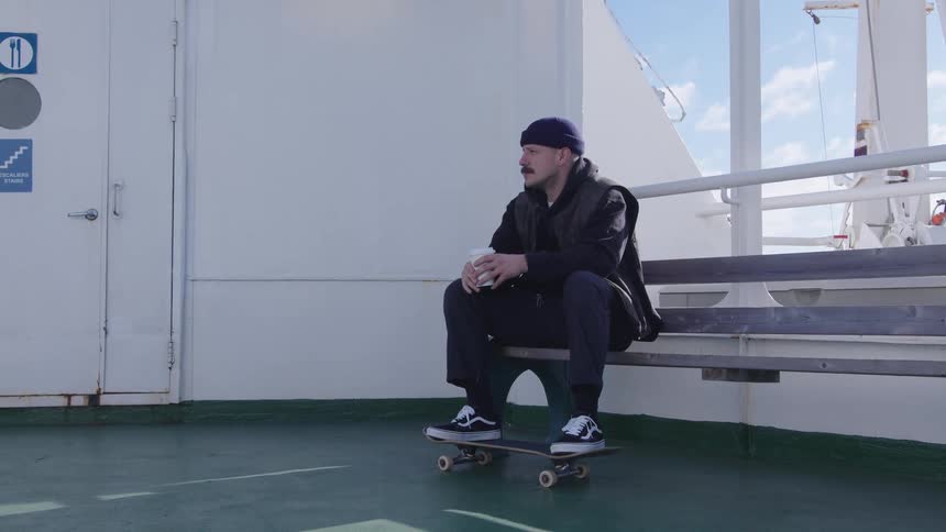 A man sits on a boat with his skateboard