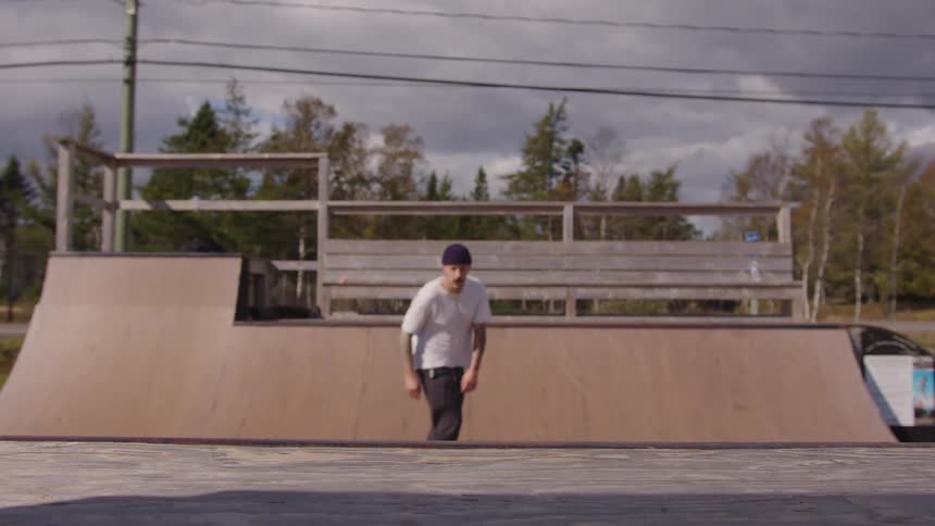 A young man rides his skateboard on a board ramp at midday in a skateboarding park