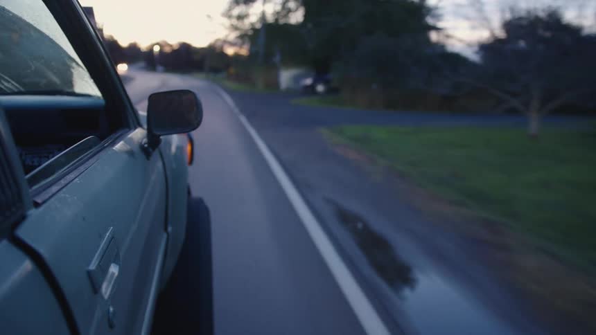 Old car drives down the road at dusk with headlights in the distance