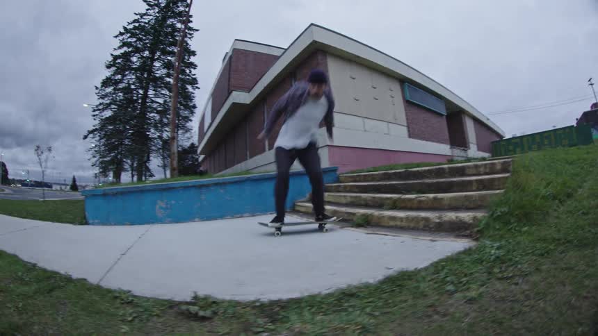 Skateboarder performs a trick over a stair set in front of a brick building