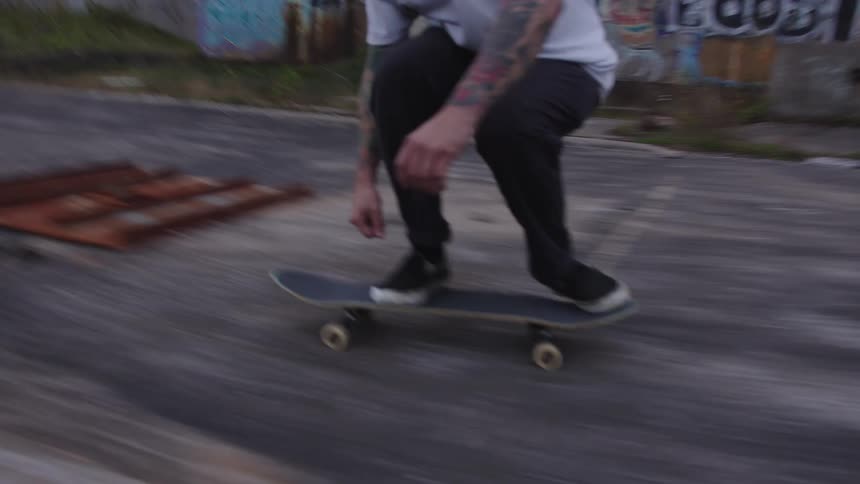 The video shows a man in a white shirt and black pants skateboarding down a small ramp off a concrete wall with colorful stylized graffiti behind him he quickly rides off the ramp onto the pavement below