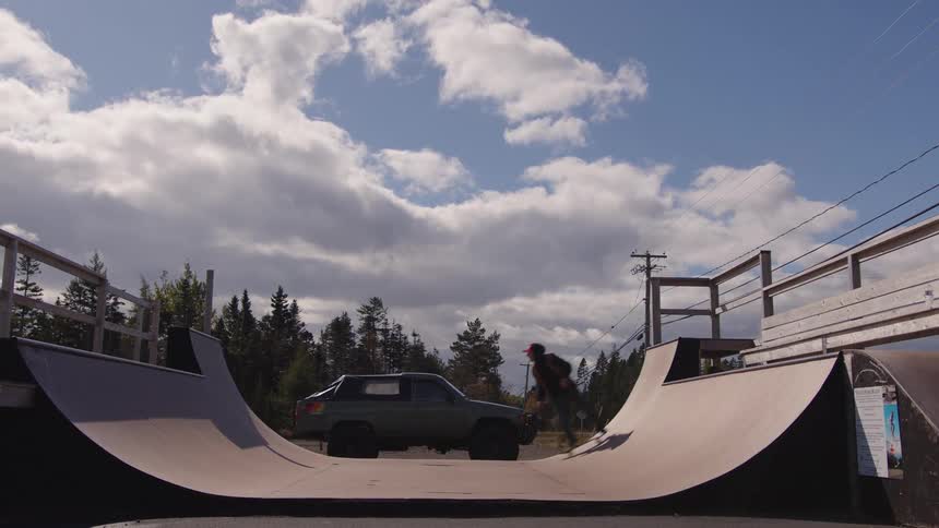 Person performing a trick on a skate ramp under a partly cloudy sky