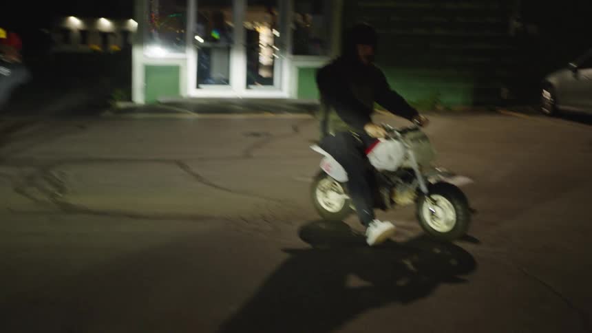 Motorcyclist performs a wheelie on a red bike at night while another watches