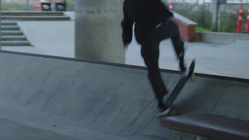 A young man wearing a black jacket rides a skateboard on a ramp at midday