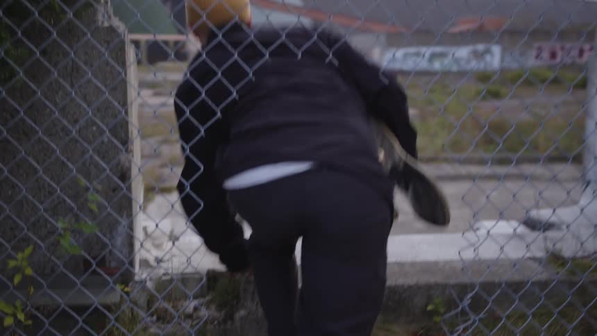 A man climbs through a fence carrying a skateboard