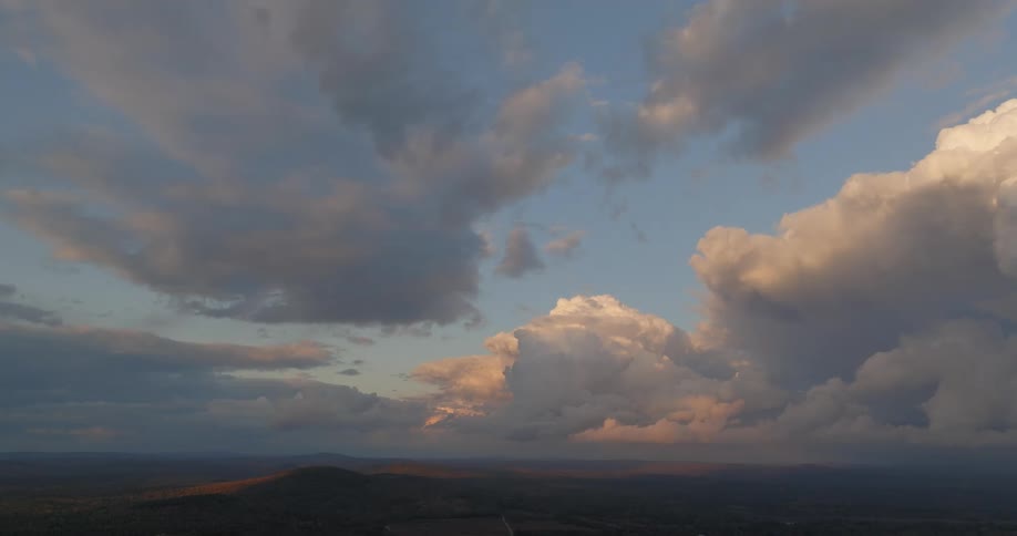 A wide sky with towering sunlit cumulonimbus and darker clouds stretches over distant hills