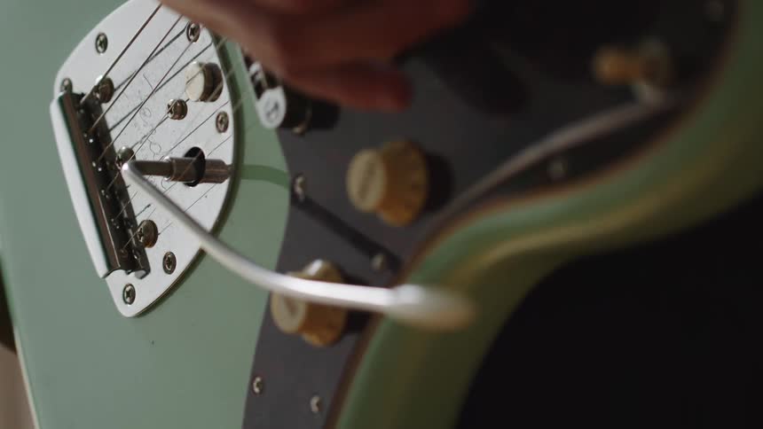 The video is a closeup of someone playing a light green electric guitar the player uses their hand to adjust a switch and then uses the whammy bar near the bridge of the instrument