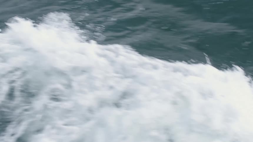 A closeup view shows the dark surface of water being violently disturbed a large volume of white foam and wake rolls away from the bottom right corner