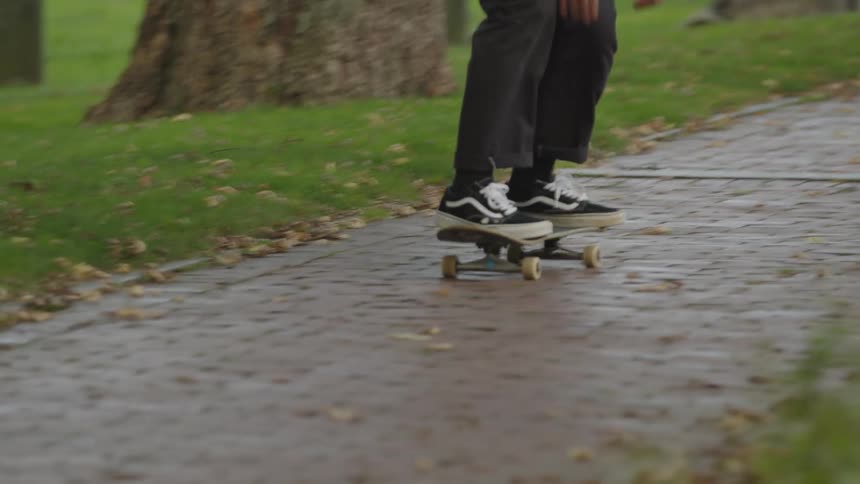 Man wearing dark clothes skateboarding in a park next to an urban area outdoors during day time
