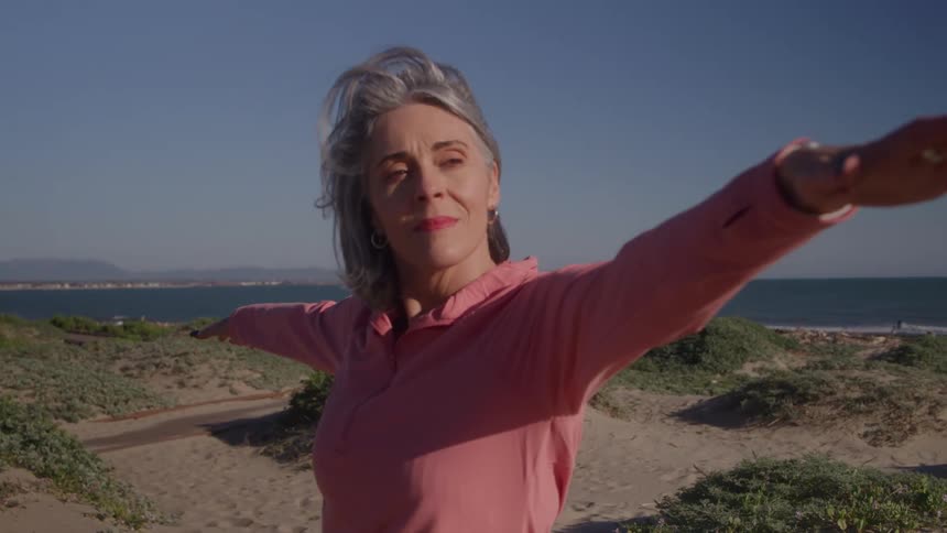 Older woman stretching with arms open on a sunny beach