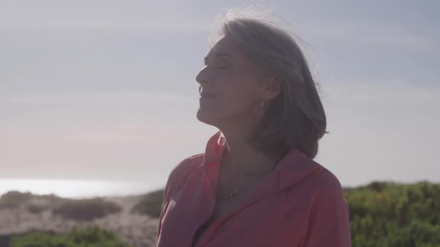 Grayhaired woman in an outdoor setting with vegetation in the background