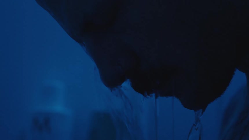 A person stands under shower in blue light