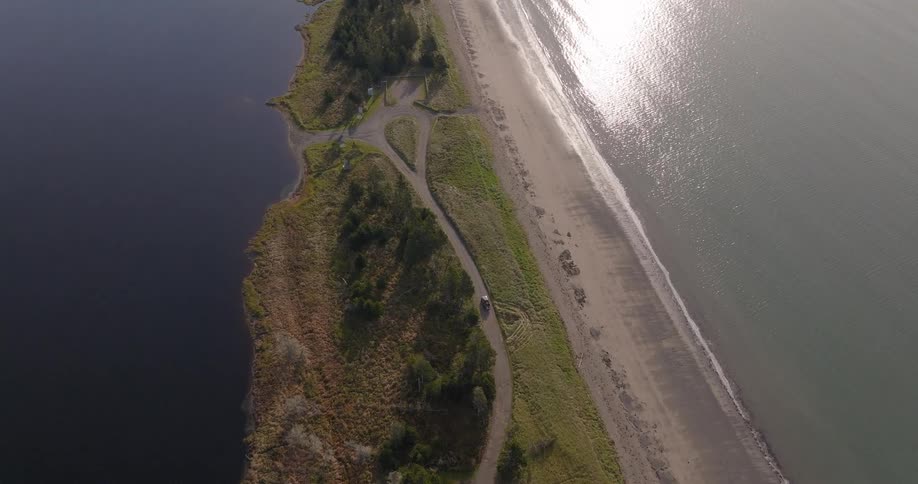 Drone view of a narrow coastline with beach and road between water