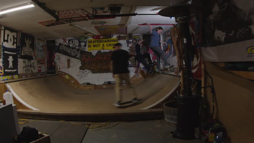 Three teenagers are skateboarding on the ramp in the garage