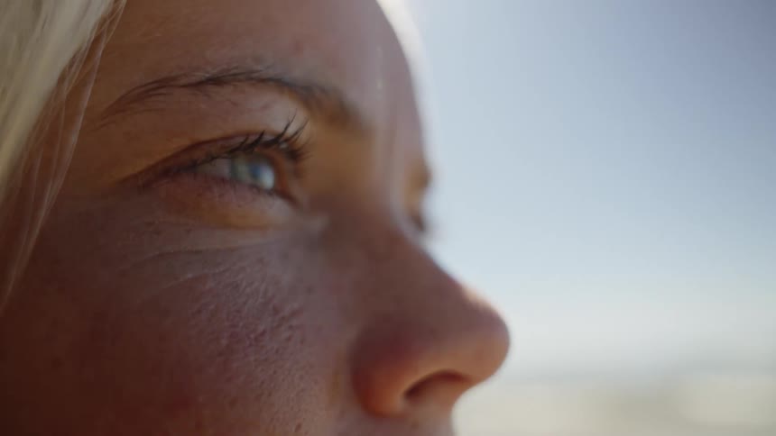 A womans face is shown in closeup profile outdoors against a clear blue sky