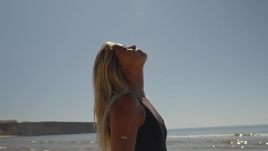 Woman in profile with blonde hair standing by the sea under clear sky