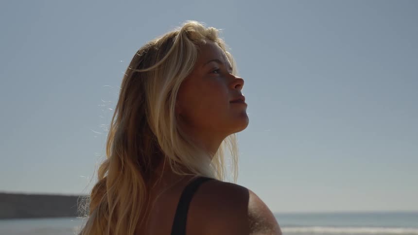 Close up portrait of a young blonde woman observing the skies while standing at the beach during daytime
