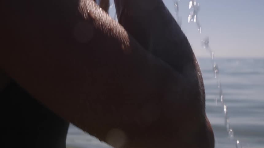 A woman in the sea water scooping up water with her hand and rubbing it on her face and body