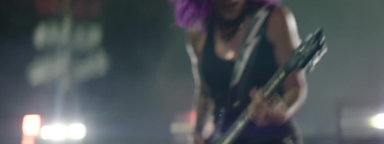 The woman is jumping around playing the guitar at night
