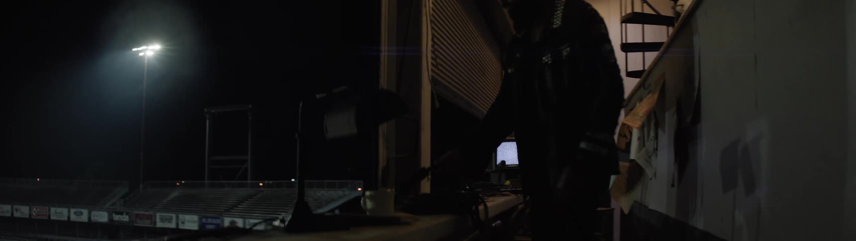 Man inside a stadium booth looking outside under night lights