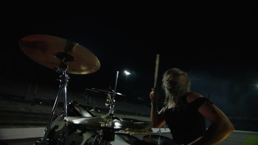 Woman with loose hair playing drums in outdoor nighttime performance radiating energy and intensity