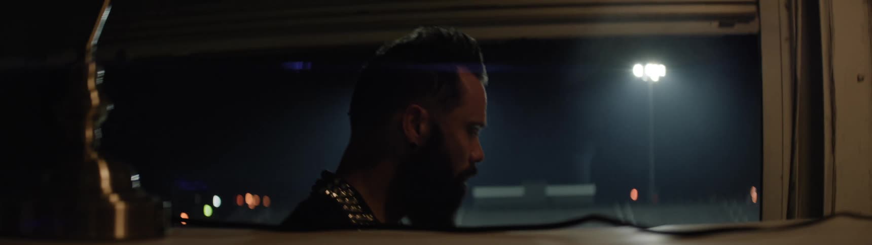 Bearded man quietly watches the empty track under the stadium lights at night