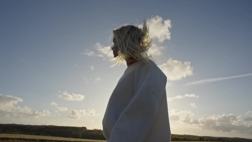 A young blonde woman walking through a field outdoors on a windy day in daytime