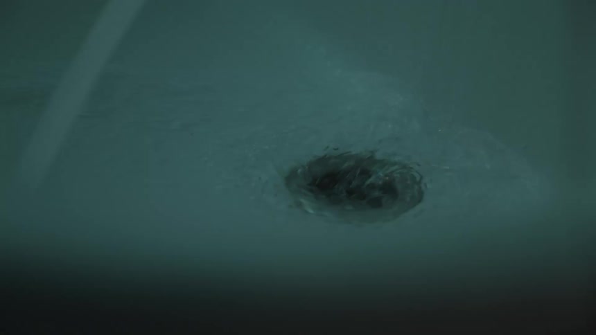 A bathtub drain swirls as water empties from a running faucet in a teallit scene