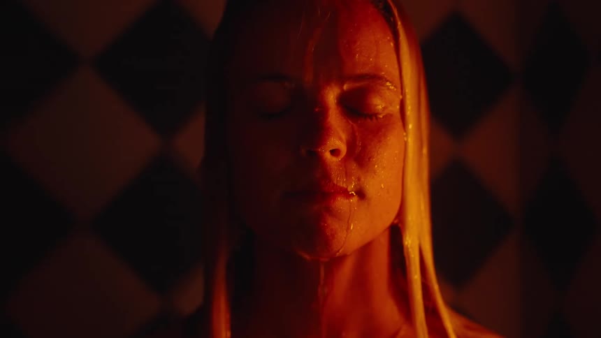 Blonde female standing in the shower in the dark as water drips down her face