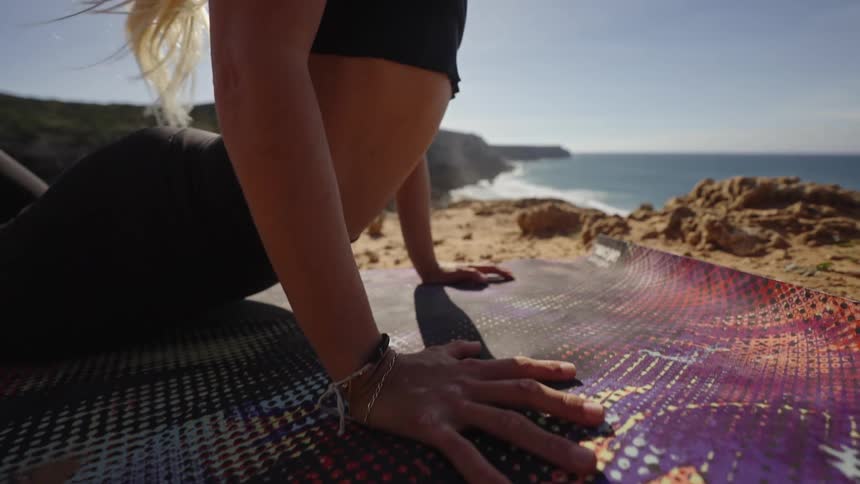 Someone performs yoga on a patterned mat outdoors bathed in dappled sunlight