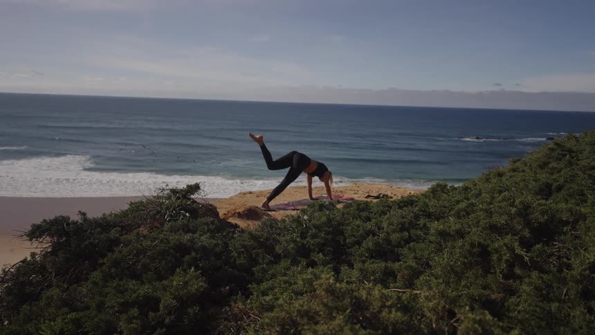 Woman practicing yoga on a cliff overlooking the ocean