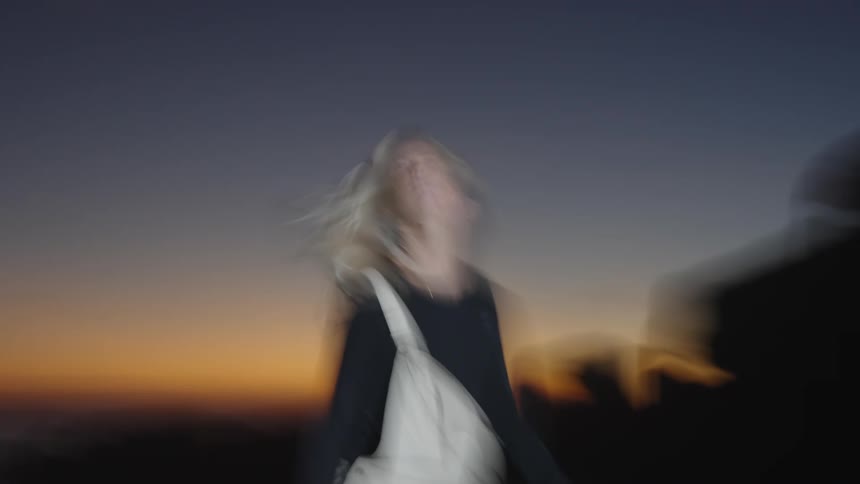 A young woman with blonde hair stands on the beach sand at dawn