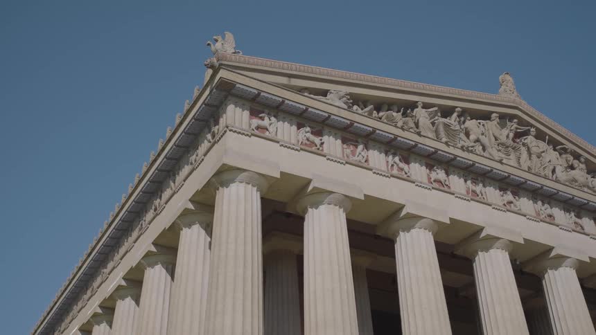Facade of a classical temple with columns and sculptures under a blue sky