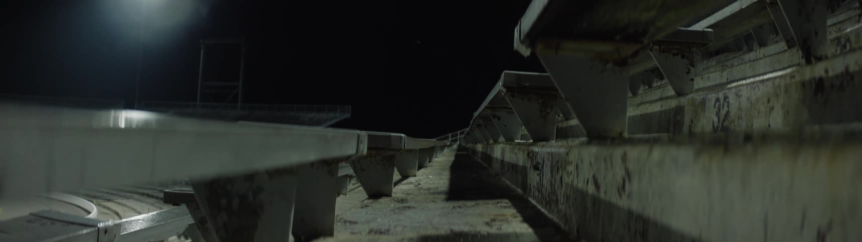 Long tiered rows of empty concrete stadium seating stretch into the distance from a lowangle perspective illuminated dimly against a pitch black night sky with a single light visible in the far background