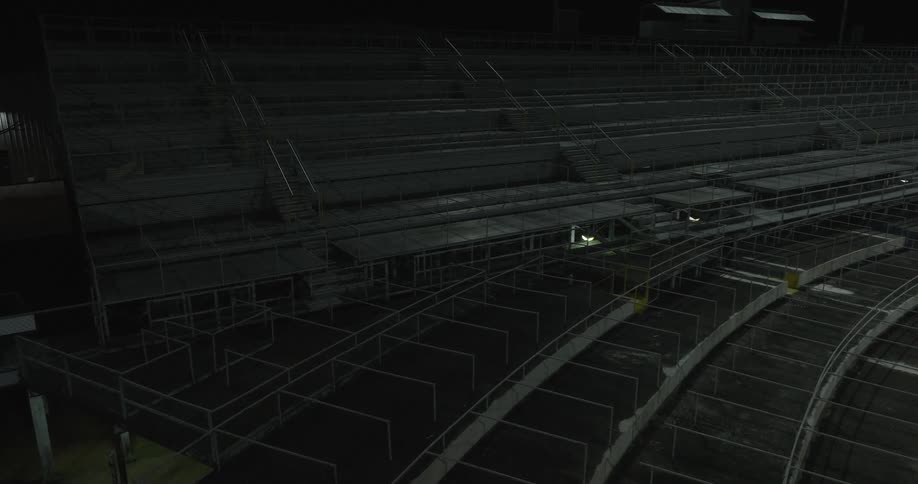 A closeup view shows the empty seating tiers of a large stadium the structure consists of concrete steps and dark metal framework the area is dimly lit and its deserted at night