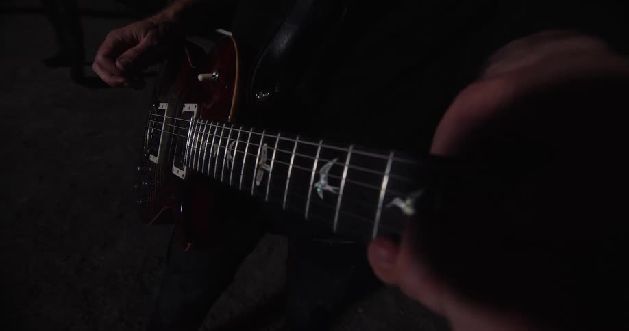 The video shows a closeup of a person playing an electric guitar the focus is on the fretboard and the players handsthe guitar has a dark red finish and the fretboard appears to have distinctive bird inlays