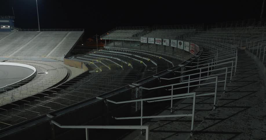 Empty metal bleachers of a racetrack illuminated by floodlights at night