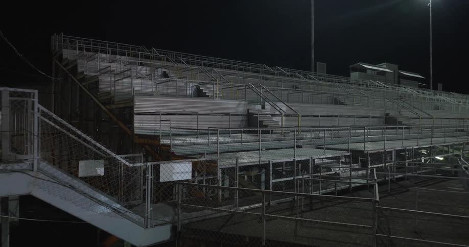 Empty metal bleachers and stairways of a stadium under night lighting
