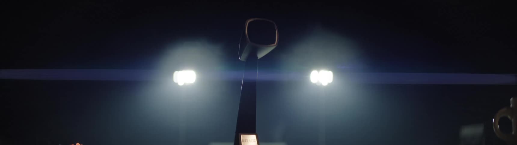 A low angle view looks up at a trophy with a square hollow top and a small base illuminated by bright stadium floodlights in a dark hazy atmosphere