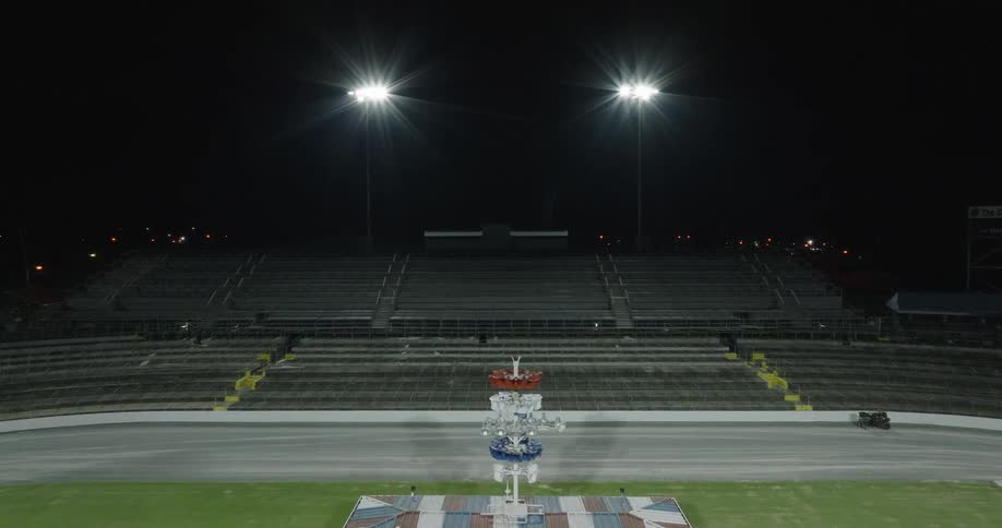 A stage is set up inside a stadium at night brightly illuminated by lights