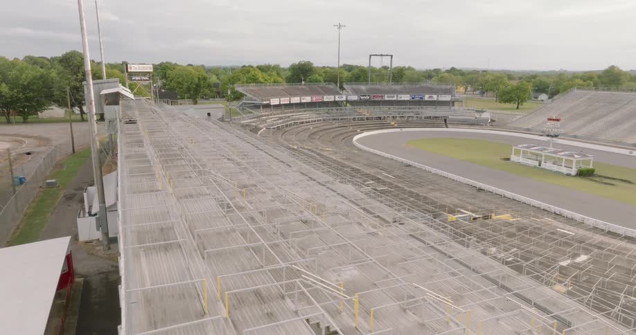 An empty roofless stadium stands under the midday sun