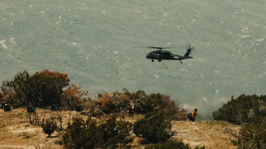 The helicopter flies over the firefighter on the mountain