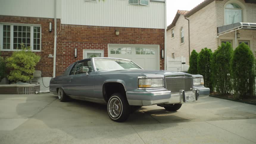 A classic lowrider with white wall tires parked in a suburban driveway
