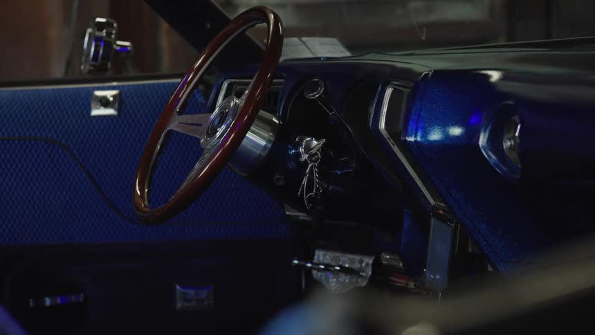 The video is an extreme closeup shot of the interior of a lowrider car highlighting the custom blue metallic flake paint on the dashboard the shot focuses on the detailed wooden steering wheel and the deep glossy custom paint finish inside