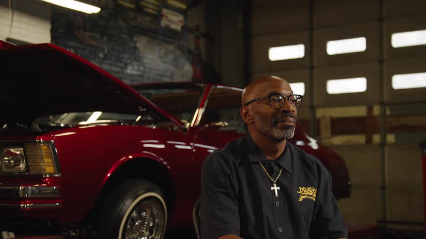 A black man sitting in a vintage auto repair workshop