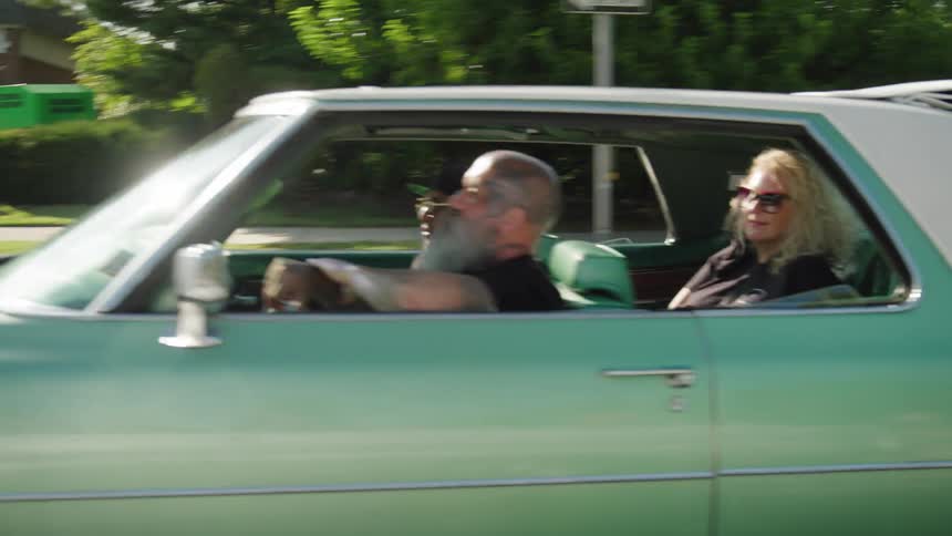 Three people ride together in a lowrider on a sunny street enjoying the drive