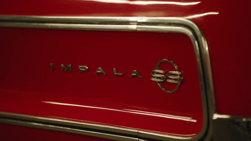 The video is an extreme closeup on the back panel of a red vintage car with a distinct metallic chrome strip running horizontally below the chrome strip the words im pala ss are visible in metal lettering identifying it as a chevrolet impala