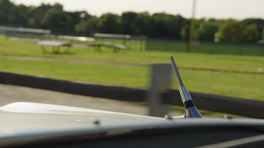 Antenna on vehicle roof in grassy area with picnic tables and fences in the background