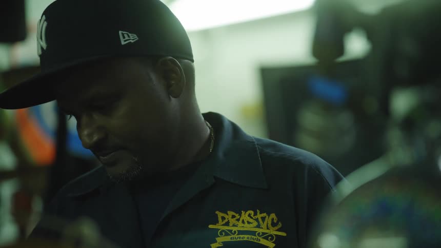 The video is a closeup shot of a man in a dark new york yankees baseball cap and a dark work shirt suggesting a casual work or urban setting he is indoors and appears to be concentrating on something just below the frame with only his dark weat